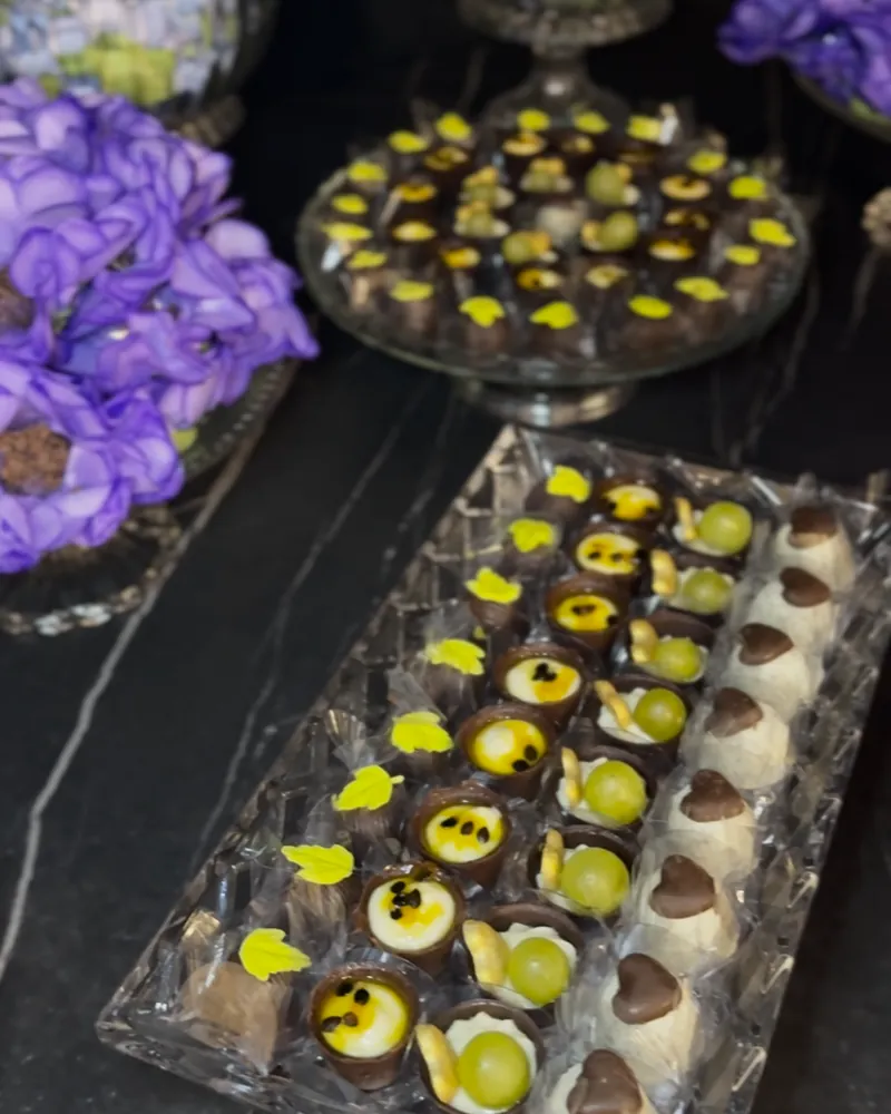 Bandeja de doces finos com detalhes amarelos e mesa decorada com flores lilás em festa de 15 anos