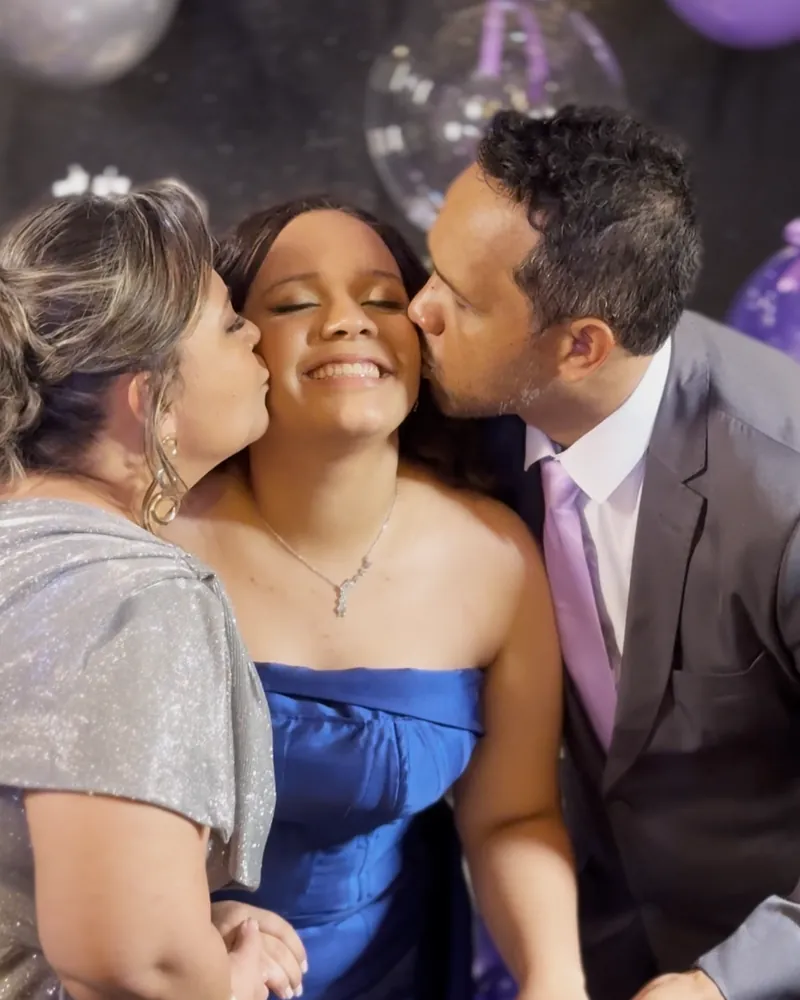 Pais beijando o rosto da debutante de vestido azul durante a festa de 15 anos