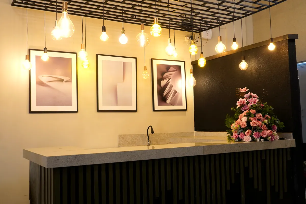 Bar do salão da Ônix Eventos com luzes pendentes amarelas, quadros na parede e arranjo de flores rosas